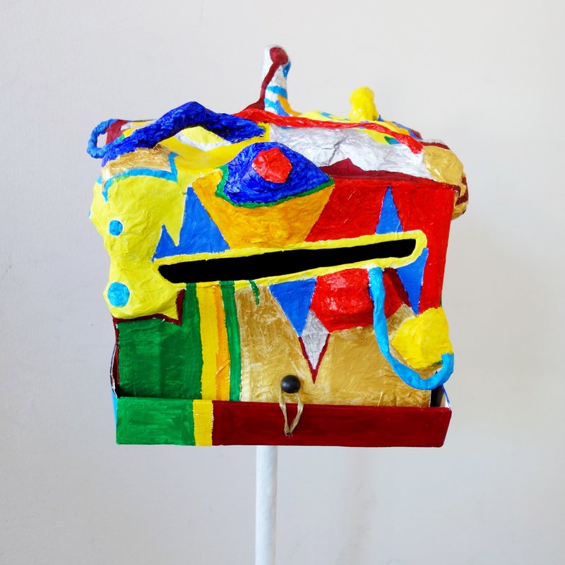 Farbenfrohe kastenförmige Skulptur mit Gesichtszügen auf Stativ