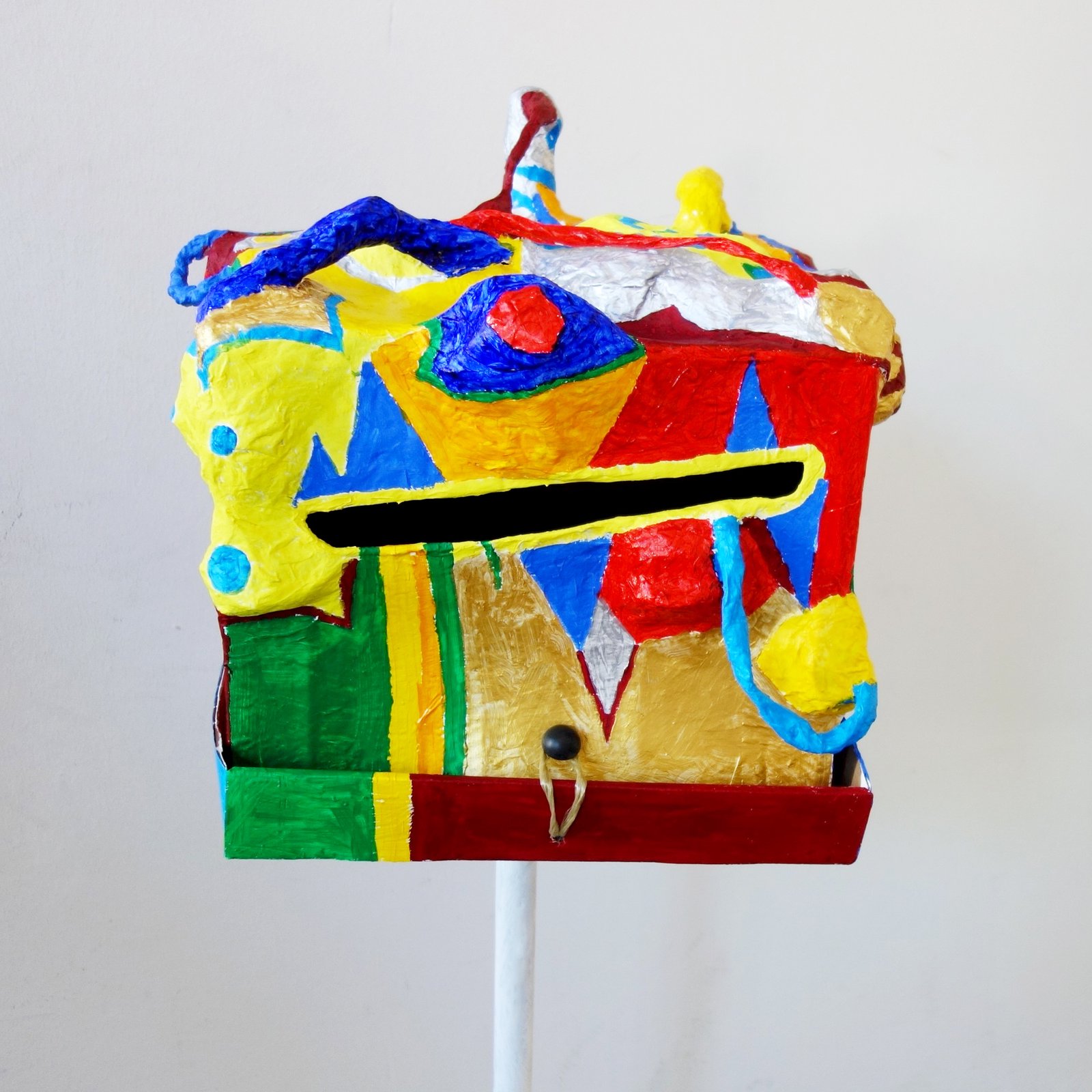 Farbenfrohe kastenförmige Skulptur mit Gesichtszügen auf Stativ