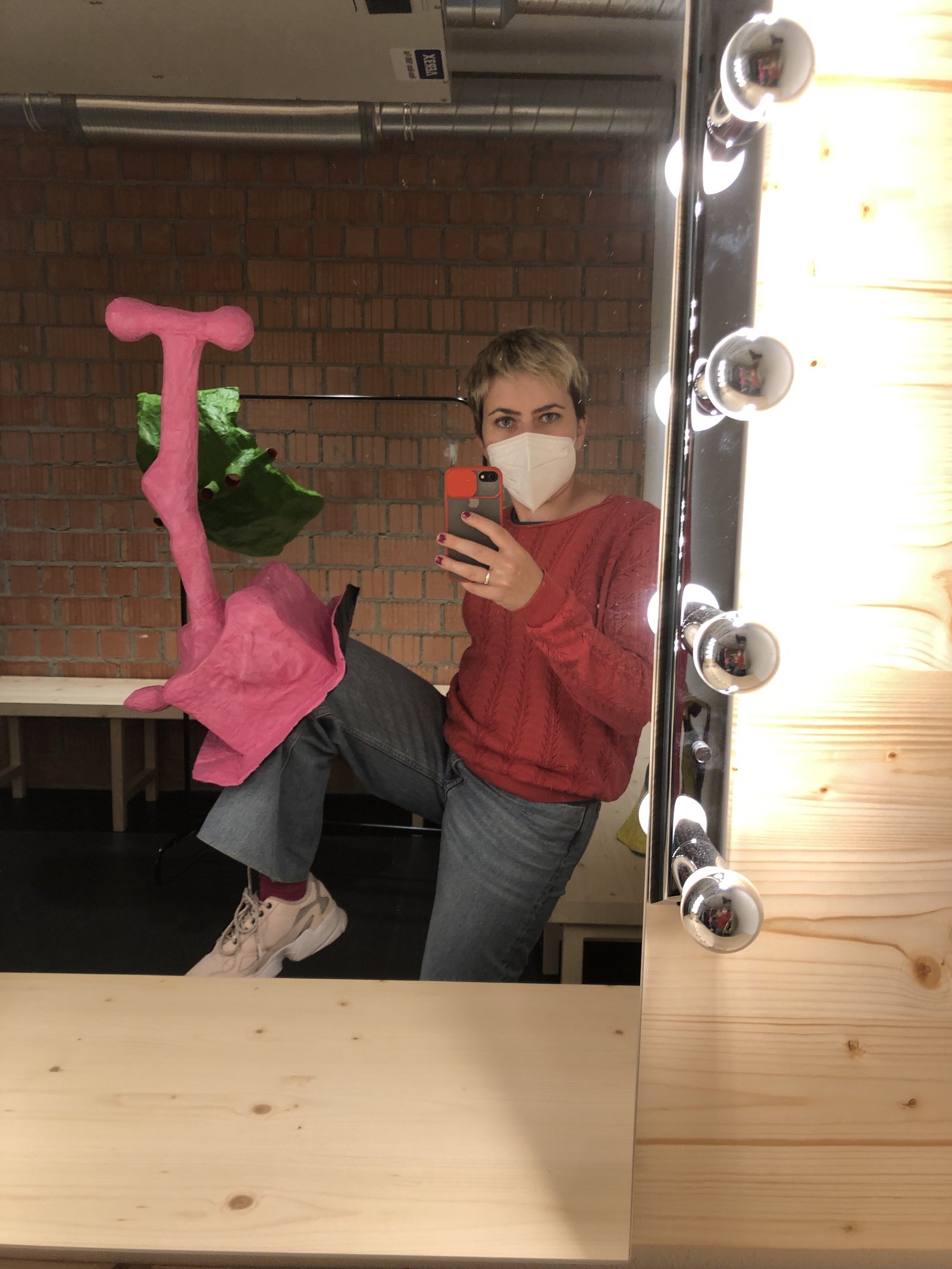 Künstlerin mit pinkfarbener Pappmaché-Skulptur vor Theaterspiegel