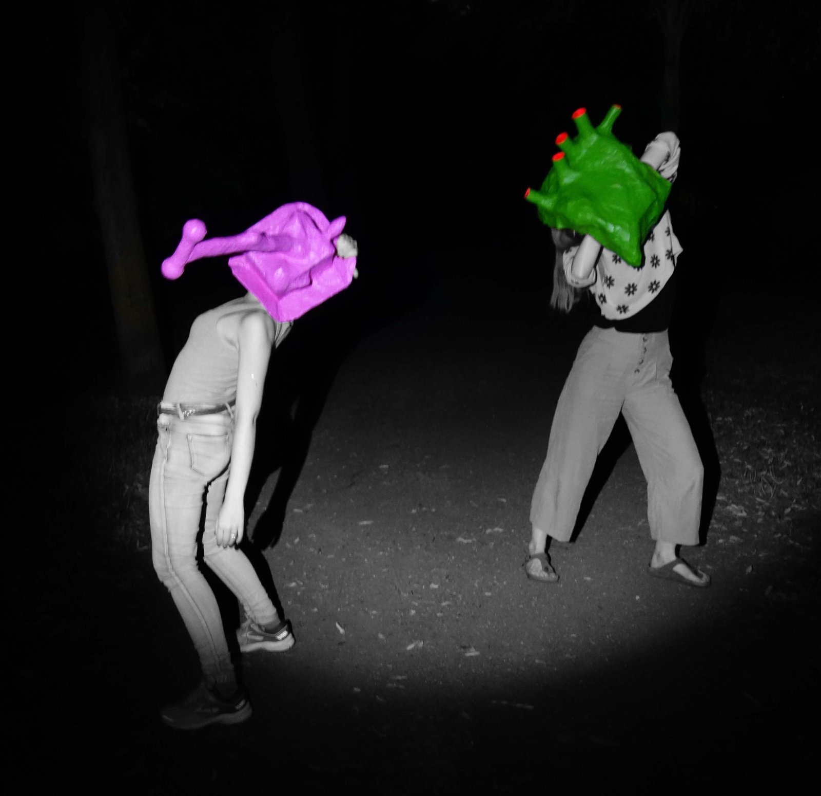 Zwei Personen mit bunten Pappmaché-Masken bei Nacht, Schwarz-Weiß mit Farbakzent