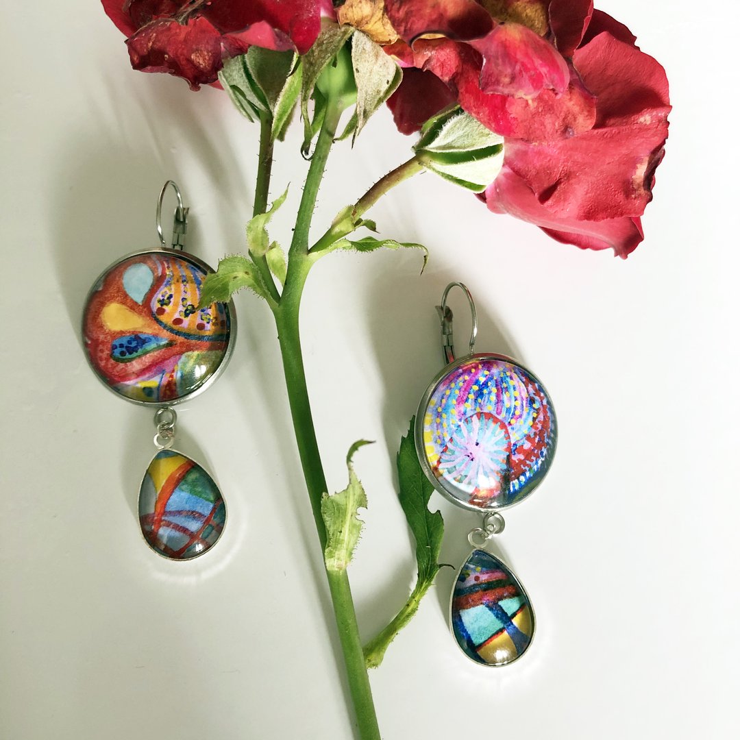 Handbemalte Glasanhänger-Ohrringe mit abstrakten Motiven neben roten Rosen