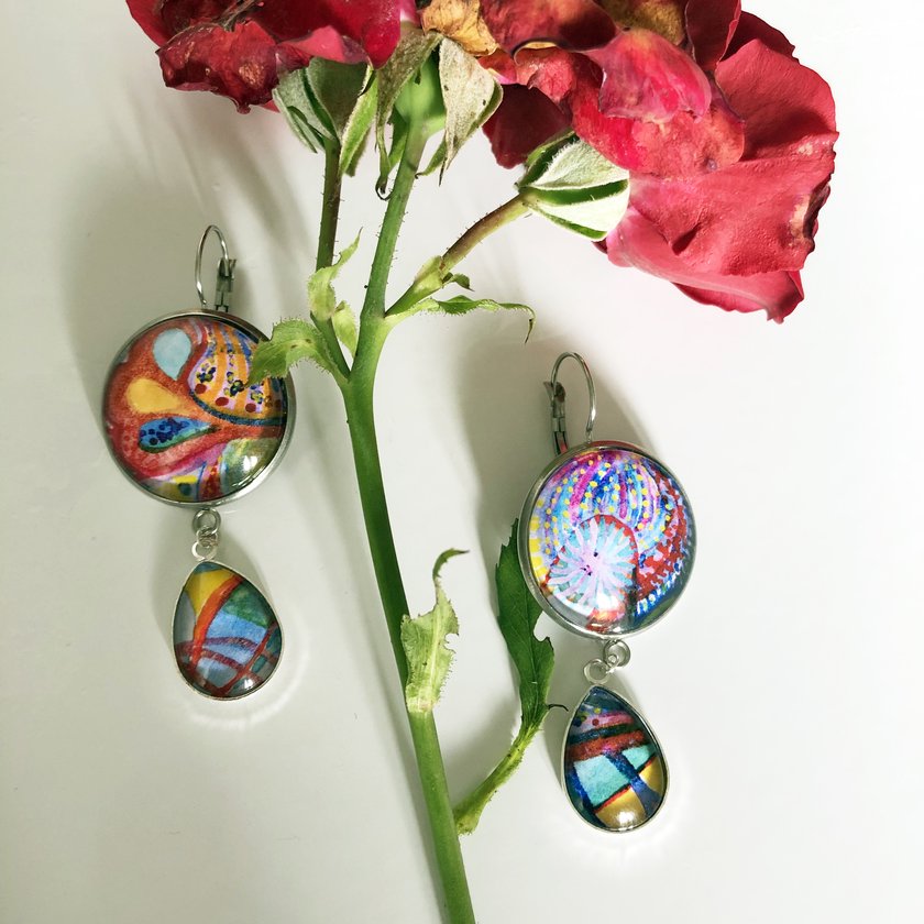 Handbemalte Glasanhänger-Ohrringe mit abstrakten Motiven neben roten Rosen
