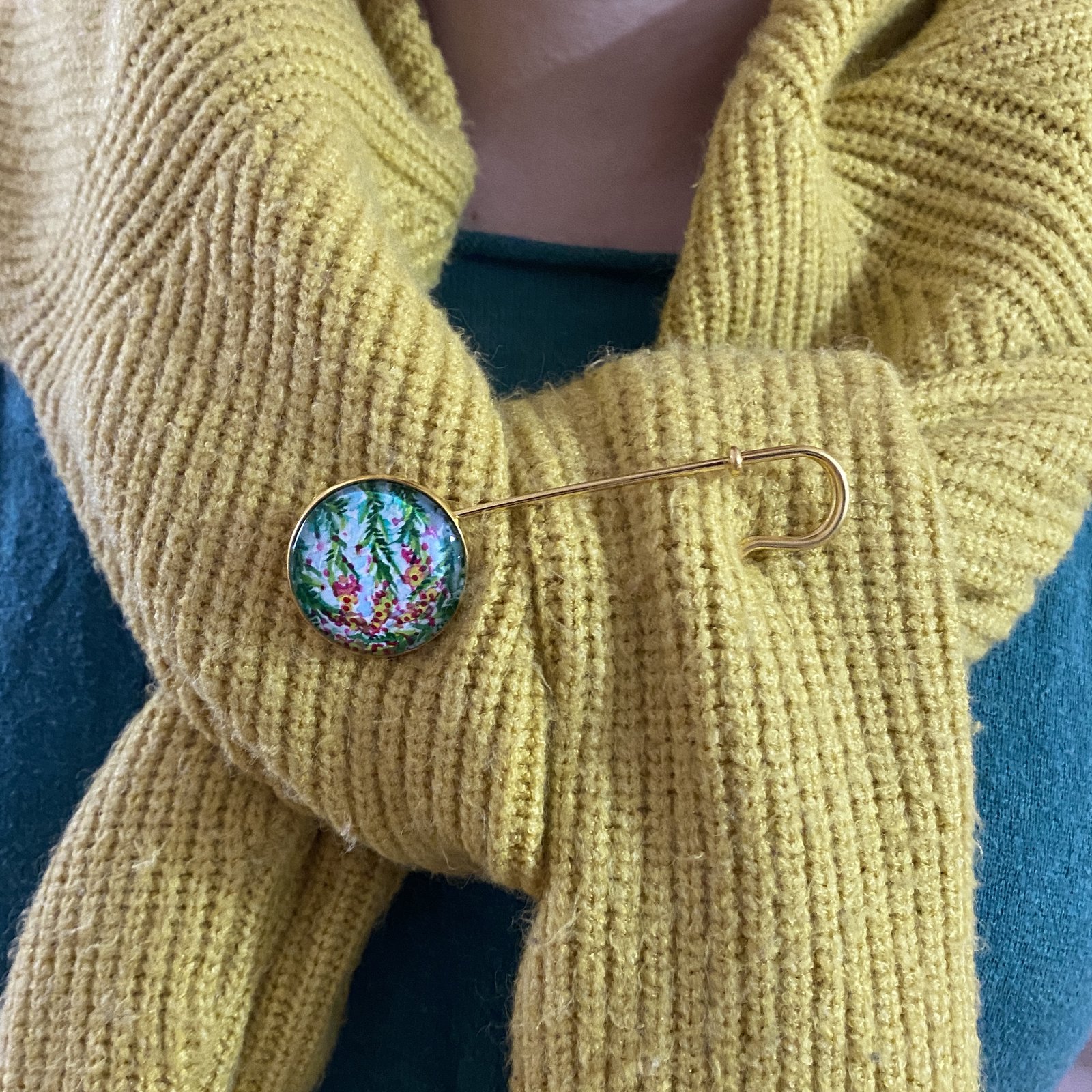 Goldene Tuchnadel mit handbemaltem Glasstein auf gelbem Strickschal